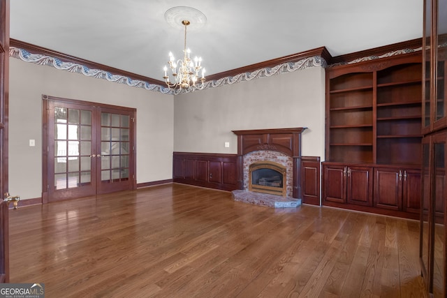 unfurnished living room with a wainscoted wall, wood finished floors, a glass covered fireplace, french doors, and crown molding