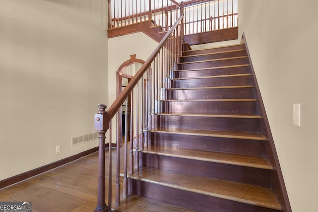 staircase featuring hardwood / wood-style floors, visible vents, baseboards, and a towering ceiling