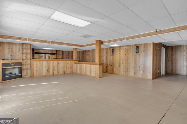 finished basement featuring a drop ceiling, wooden walls, and a fireplace