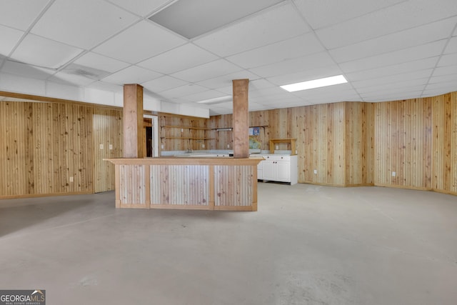 kitchen with finished concrete flooring, baseboards, a drop ceiling, light countertops, and wood walls