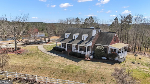 exterior space featuring a front lawn, fence, covered porch, a wooded view, and a chimney