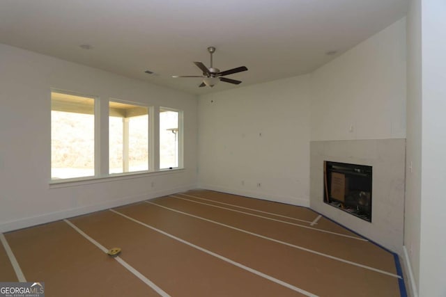 unfurnished living room featuring a tiled fireplace, visible vents, a ceiling fan, and baseboards