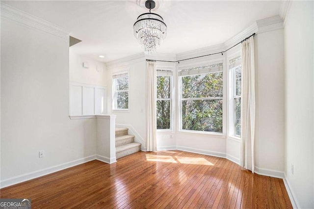 empty room featuring ornamental molding, hardwood / wood-style floors, stairway, baseboards, and a chandelier