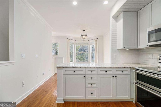 kitchen with light wood-type flooring, stainless steel appliances, a peninsula, decorative backsplash, and baseboards