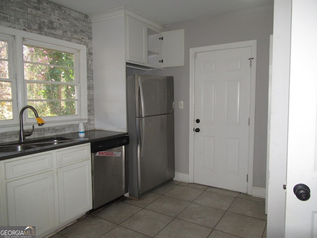 kitchen featuring light tile patterned floors, a sink, appliances with stainless steel finishes, white cabinetry, and dark countertops