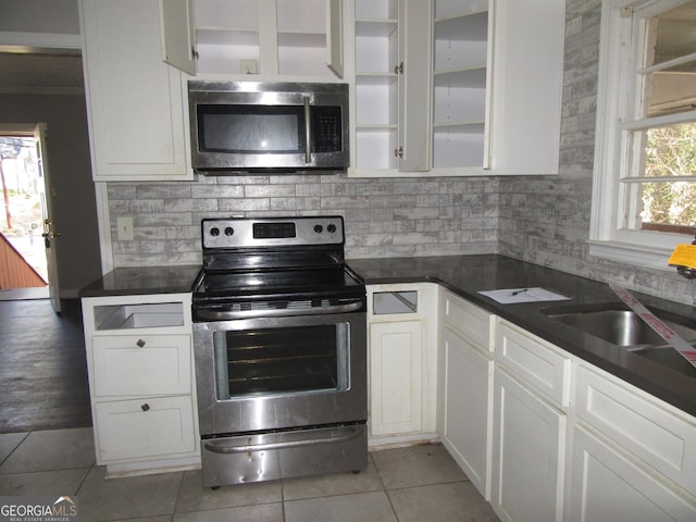 kitchen with dark countertops, appliances with stainless steel finishes, white cabinets, light tile patterned floors, and decorative backsplash