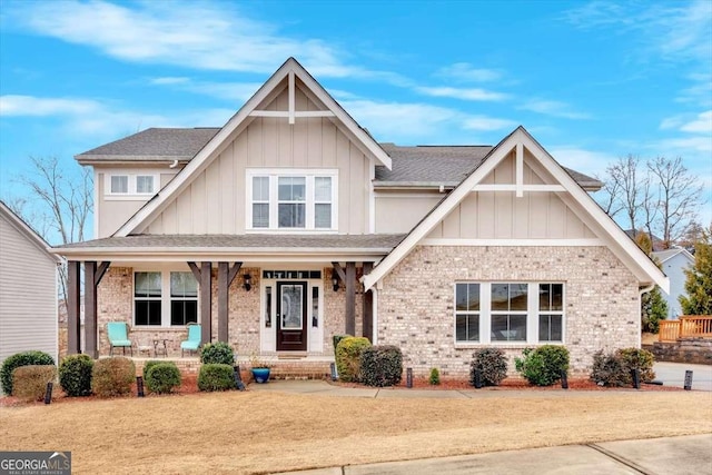 craftsman house with brick siding, covered porch, board and batten siding, and a shingled roof