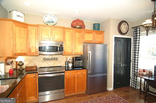 kitchen featuring dark wood-style floors, a sink, appliances with stainless steel finishes, a notable chandelier, and tasteful backsplash