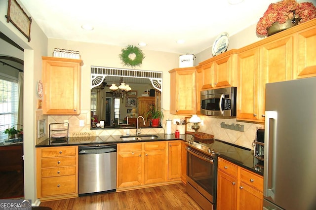 kitchen with a sink, stainless steel appliances, wood finished floors, and decorative backsplash