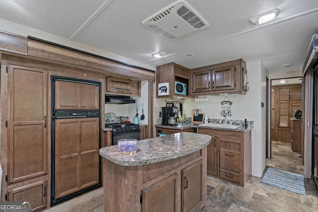 kitchen featuring a sink, under cabinet range hood, a center island, stone finish floor, and black range with gas cooktop