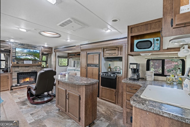 kitchen with range, a sink, a kitchen island, under cabinet range hood, and a fireplace