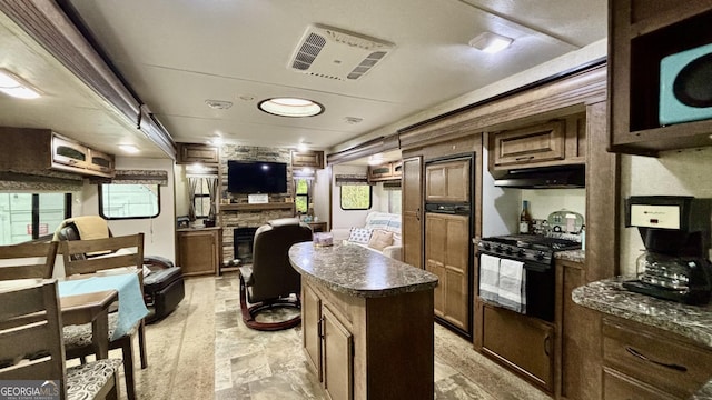 kitchen with visible vents, a fireplace, black range with gas stovetop, under cabinet range hood, and dark countertops