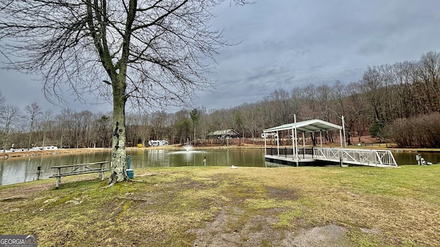 view of dock featuring a yard, a wooded view, and a water view