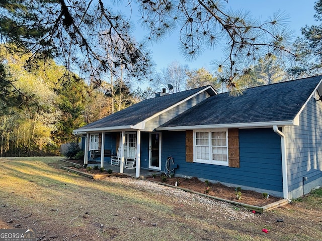 ranch-style home featuring a porch, a chimney, a front lawn, and roof with shingles