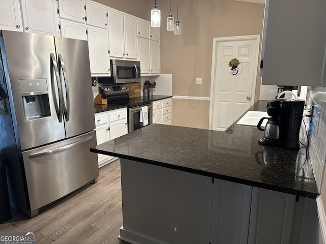 kitchen with light wood finished floors, a peninsula, stainless steel appliances, decorative backsplash, and white cabinetry