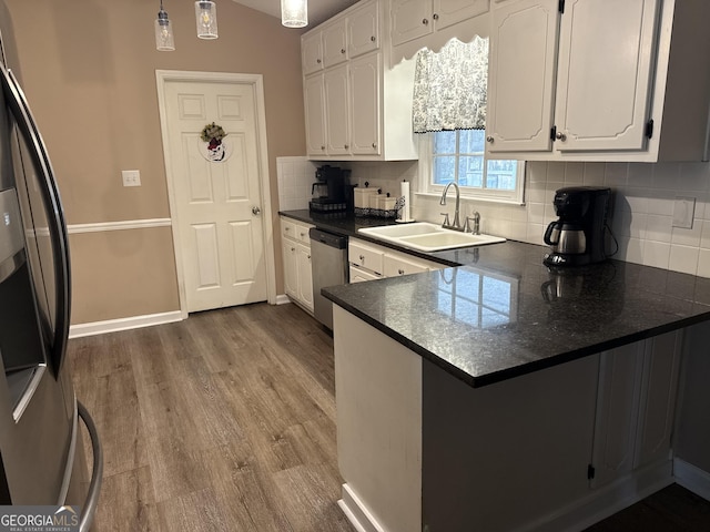 kitchen featuring dark countertops, a peninsula, stainless steel appliances, white cabinetry, and a sink