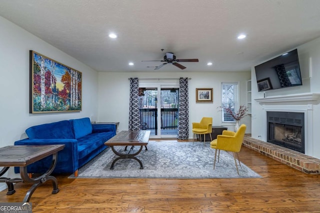 living room with a fireplace with raised hearth, built in shelves, recessed lighting, wood finished floors, and a textured ceiling