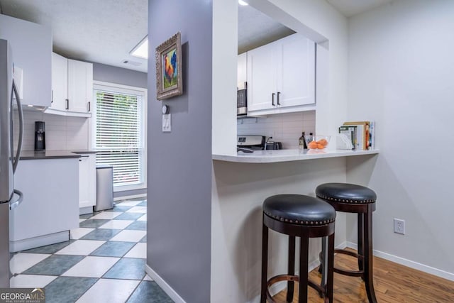 kitchen featuring a breakfast bar area, baseboards, white cabinetry, stainless steel microwave, and range