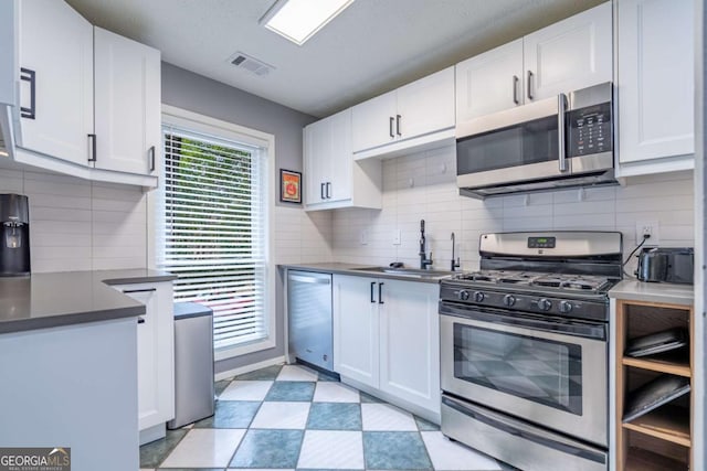 kitchen with dark countertops, visible vents, light floors, appliances with stainless steel finishes, and white cabinetry