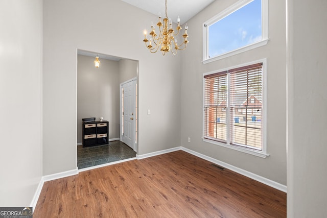 empty room with a chandelier, baseboards, wood finished floors, and a towering ceiling