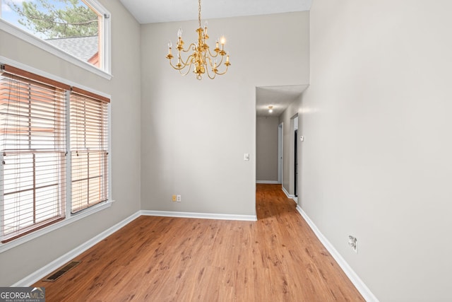 interior space featuring light wood-type flooring, visible vents, an inviting chandelier, baseboards, and a towering ceiling