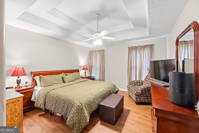 bedroom with light wood finished floors, ceiling fan, a tray ceiling, and ornamental molding