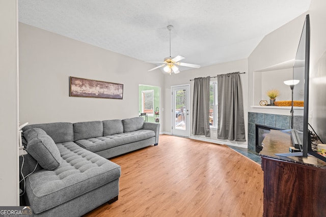 living area with ceiling fan, vaulted ceiling, a fireplace, wood finished floors, and a textured ceiling