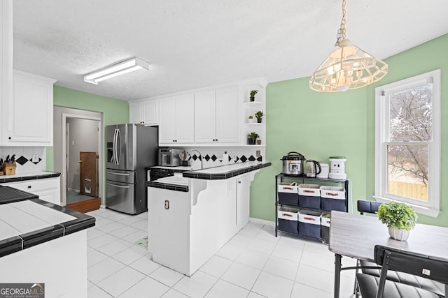 kitchen with backsplash, white cabinetry, tile countertops, a peninsula, and stainless steel fridge with ice dispenser