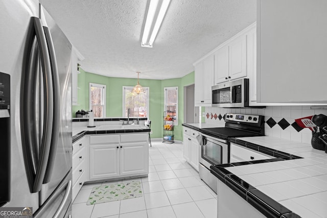 kitchen featuring a peninsula, tile countertops, white cabinets, and stainless steel appliances