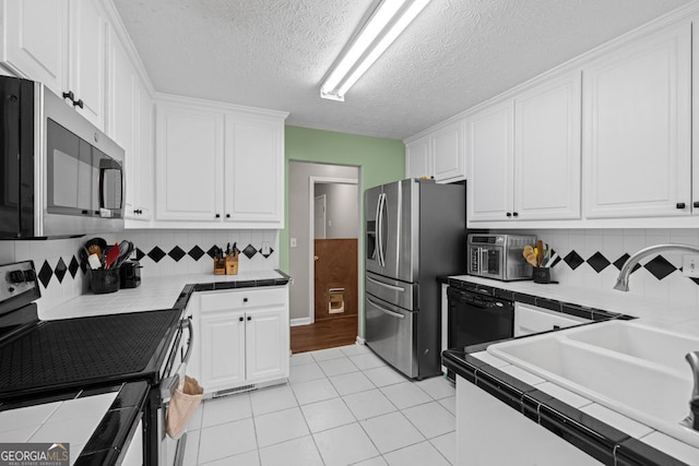 kitchen with light tile patterned floors, a sink, tile counters, white cabinets, and appliances with stainless steel finishes