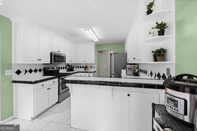 kitchen with tile counters, appliances with stainless steel finishes, a peninsula, white cabinetry, and open shelves