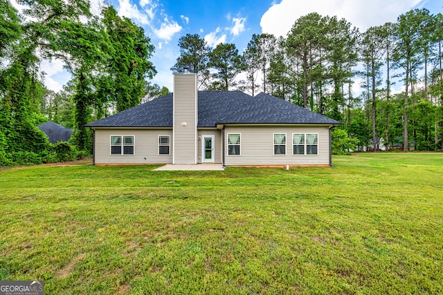 rear view of property featuring a yard, a chimney, a shingled roof, and a patio area