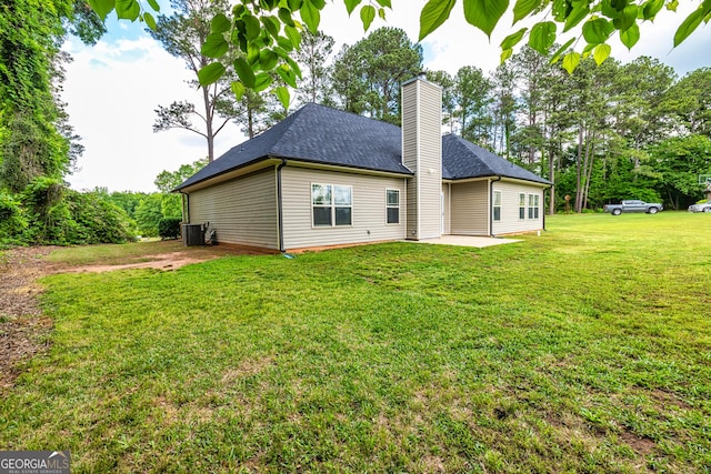 rear view of house with roof with shingles, a chimney, central air condition unit, a patio, and a yard