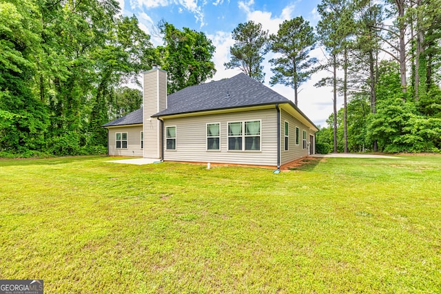 rear view of property featuring a patio, a shingled roof, a yard, and a chimney