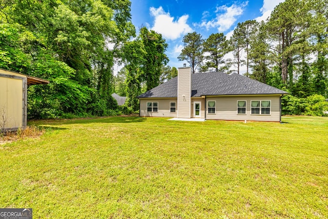 rear view of property with a lawn, a chimney, and a shingled roof