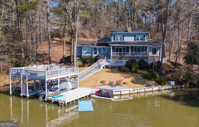 rear view of property featuring a deck with water view, boat lift, a chimney, and stairs