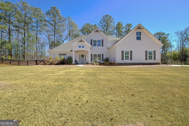 view of front of home featuring a front lawn, fence, board and batten siding, and roof with shingles