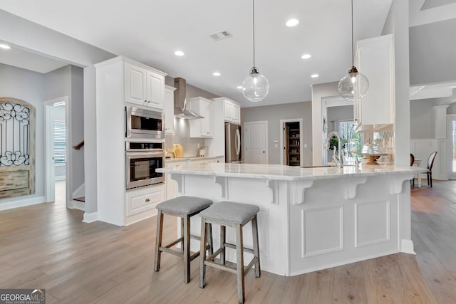 kitchen with wall chimney range hood, visible vents, a sink, appliances with stainless steel finishes, and a kitchen breakfast bar