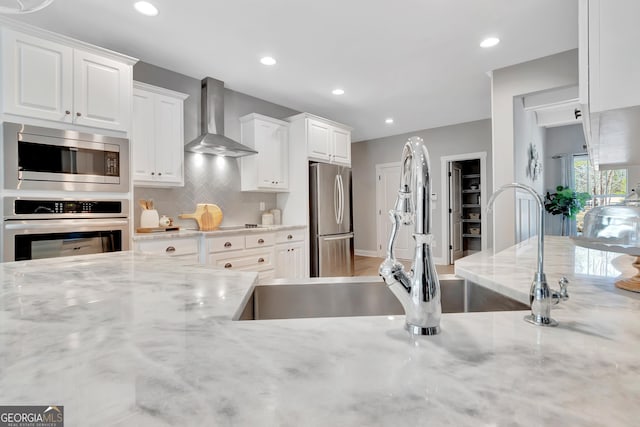 kitchen with decorative backsplash, white cabinets, wall chimney exhaust hood, and appliances with stainless steel finishes