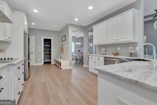 kitchen featuring a sink, white cabinetry, light wood-style floors, appliances with stainless steel finishes, and wall chimney range hood