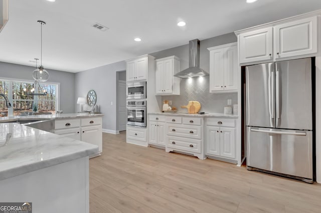 kitchen featuring visible vents, stainless steel appliances, white cabinetry, wall chimney range hood, and light wood-type flooring