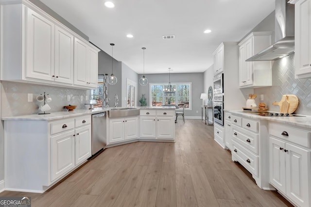 kitchen with visible vents, a peninsula, a sink, stainless steel appliances, and wall chimney exhaust hood