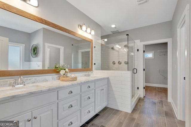 full bathroom with double vanity, a stall shower, wood tiled floor, and a sink