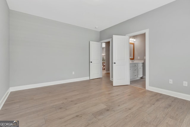 unfurnished bedroom with lofted ceiling, ensuite bathroom, light wood-type flooring, and baseboards