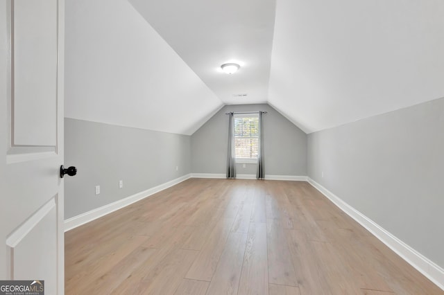 additional living space featuring vaulted ceiling, light wood-style floors, and baseboards