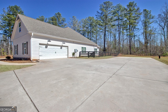 view of side of home with a garage, roof with shingles, and concrete driveway