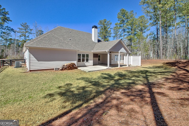 back of house featuring a lawn, central AC, a shingled roof, a chimney, and a patio area