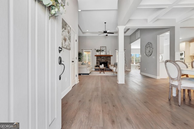 foyer with light wood finished floors, beam ceiling, a fireplace, and a ceiling fan