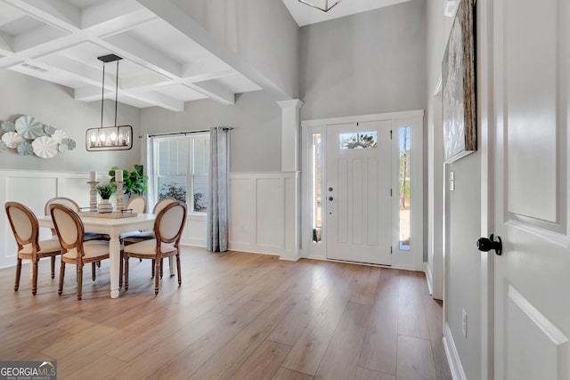 foyer with a wainscoted wall, coffered ceiling, light wood finished floors, beamed ceiling, and a notable chandelier