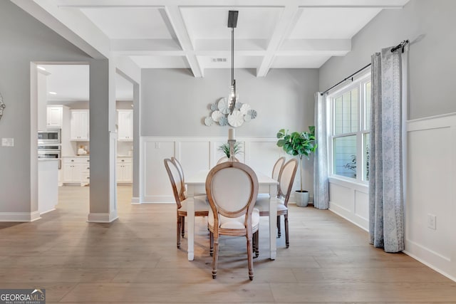 dining area featuring beam ceiling, light wood-style flooring, coffered ceiling, an inviting chandelier, and a decorative wall